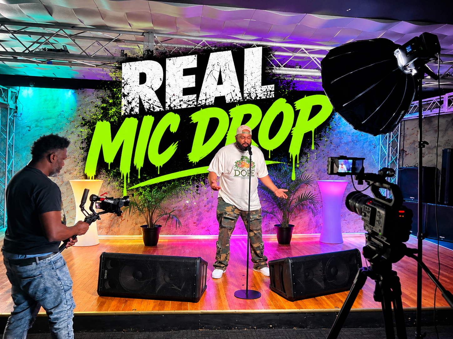 The Real Mic Drop — live stage performance with camera crew, stage lighting, and REAL MIC DROP backdrop