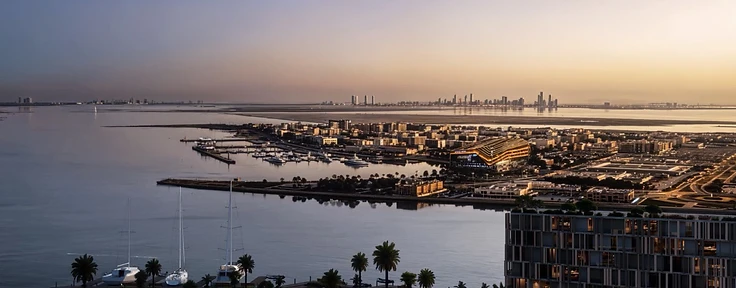 Dusk render of the Wadi waterfront with a lit residential facade, palm-lined curved promenade, docked sailboats and a distant Abu Dhabi skyline at sunset
