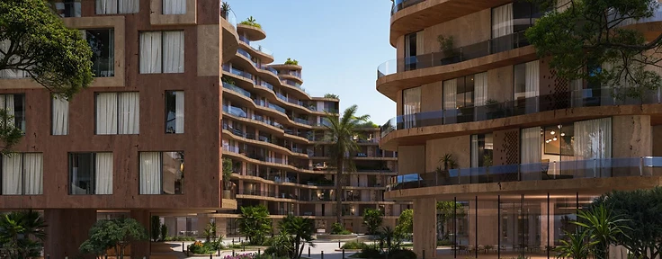 Landscaped courtyard between two Wadi residential buildings — terracotta grid facade on one side and curved beige balconies on the other, with palm trees and flowering shrubs