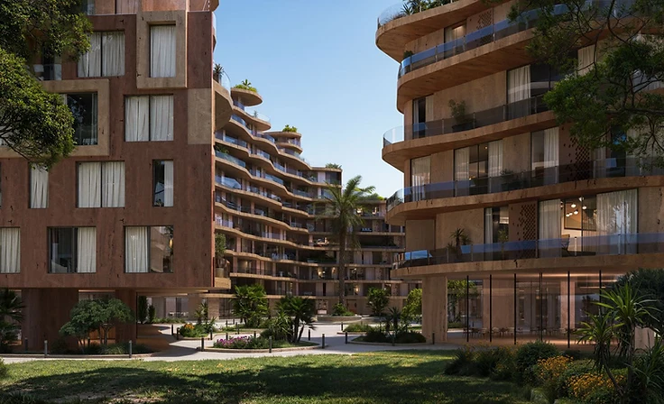 Landscaped courtyard between two Wadi residential buildings — terracotta grid facade on one side and curved beige balconies on the other, with palm trees and flowering shrubs