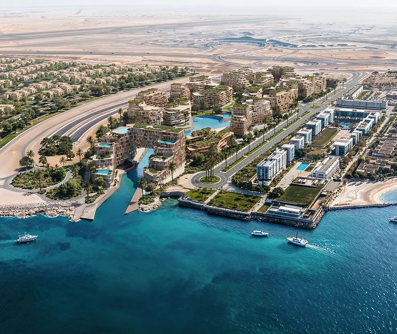 High-angle aerial render of the Wadi community on Yas Island showing a teal lagoon cutting between organic beige residential blocks, a beach and desert terrain beyond