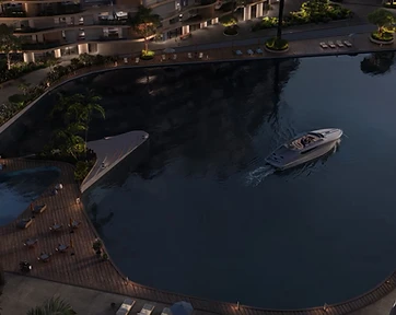 Night aerial render of the Wadi lagoon with warm lit boardwalk lounges, curved residential facades glowing from within and a speedboat crossing the dark water