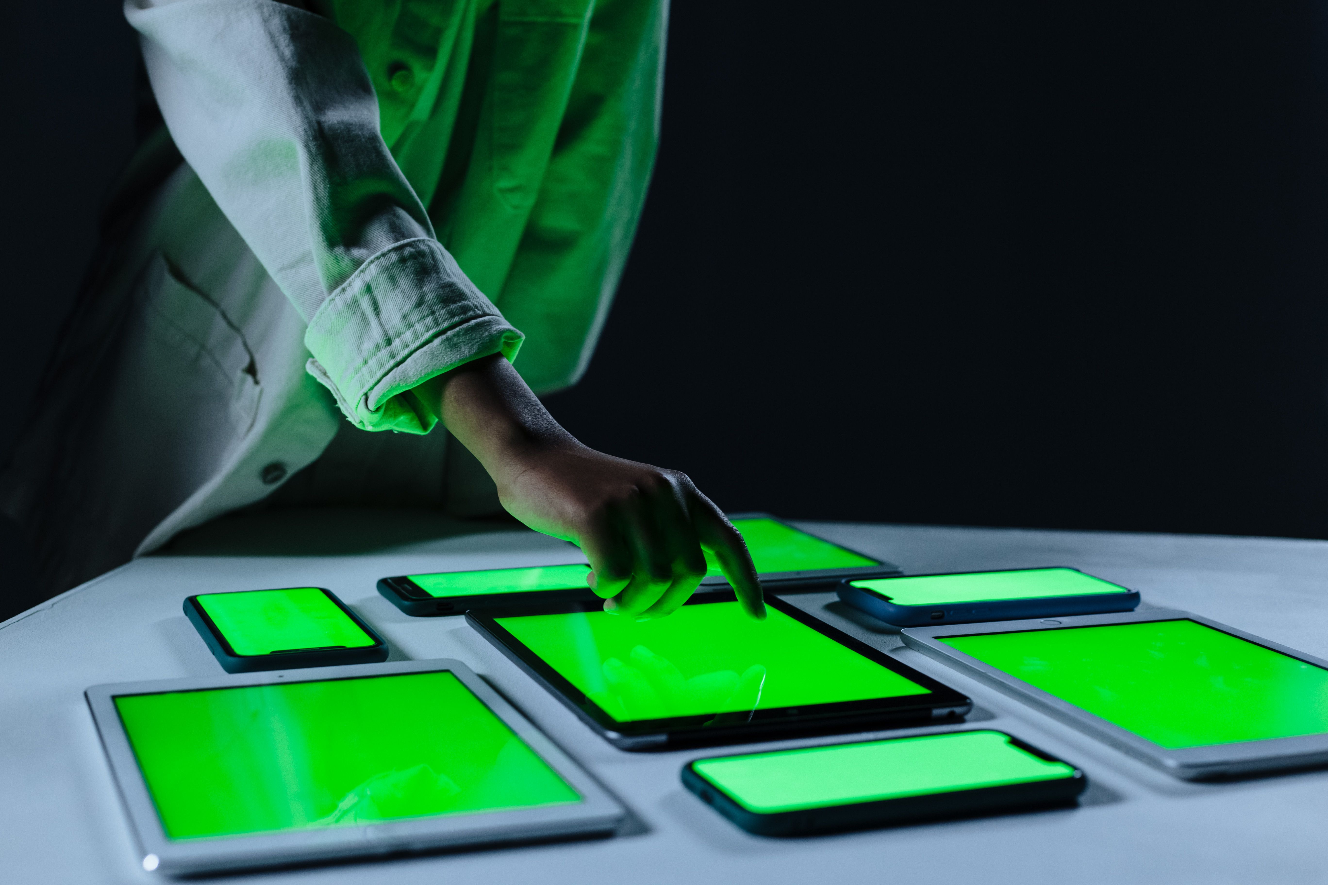 A hand reaching for tablets and phones with glowing green screens