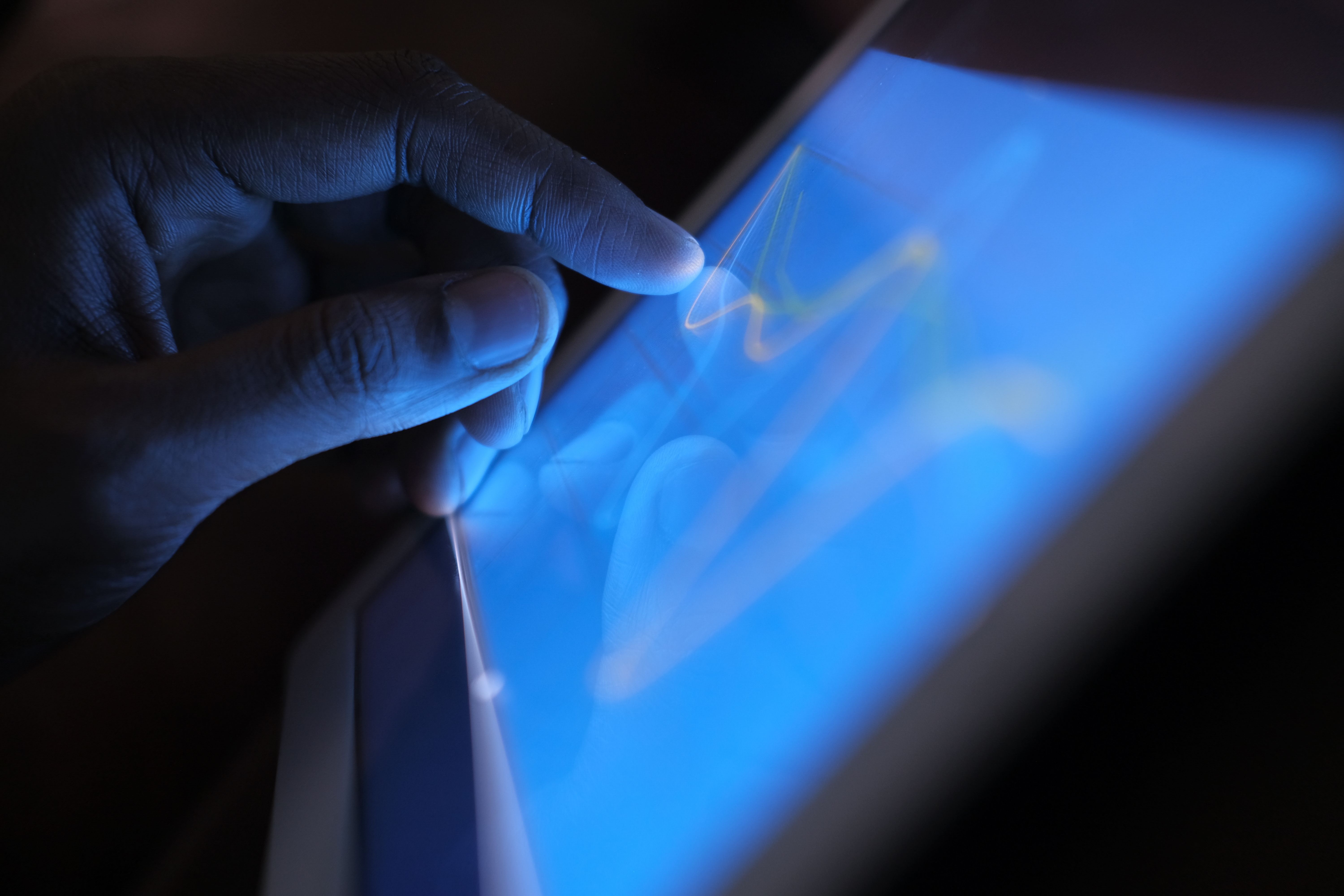A finger touching a glowing blue tablet screen