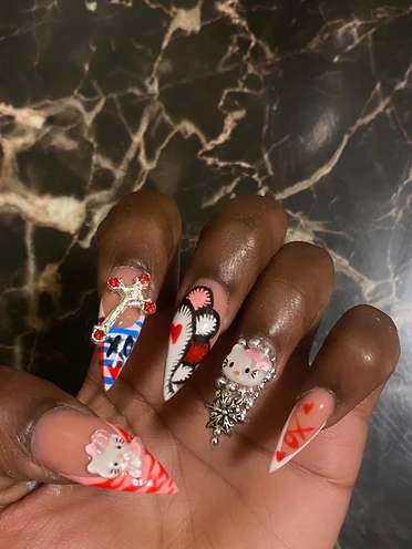 Long stiletto acrylics with 3D Hello Kitty figures, zebra stripes, silver cross charms, and rhinestone detailing.