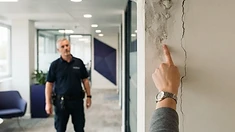 Hand zeigt auf einen Wasserschaden und Riss an der Wand in einem Bürogang