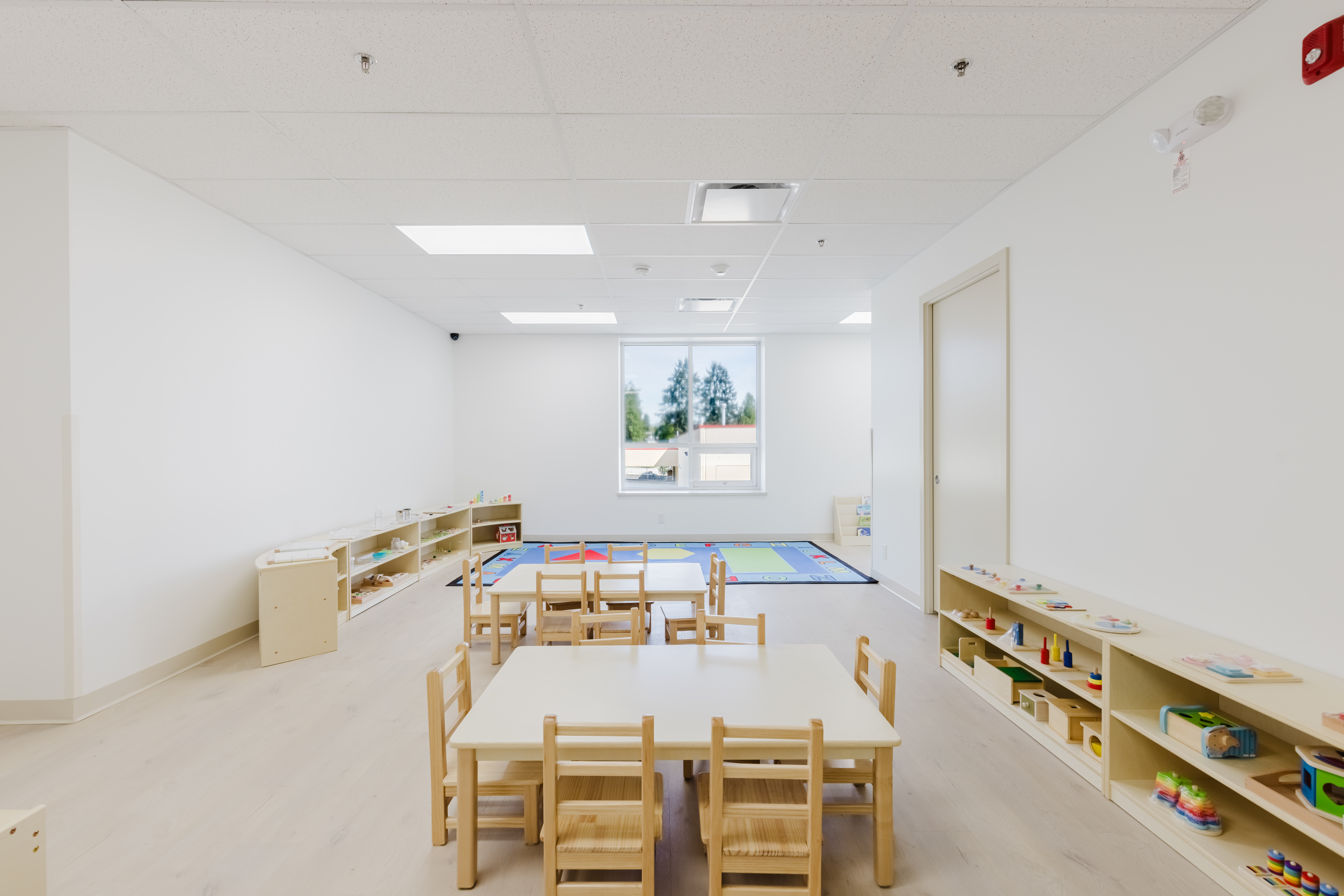 Light-filled toddler classroom with alphabet rug and open shelving at Kidzville