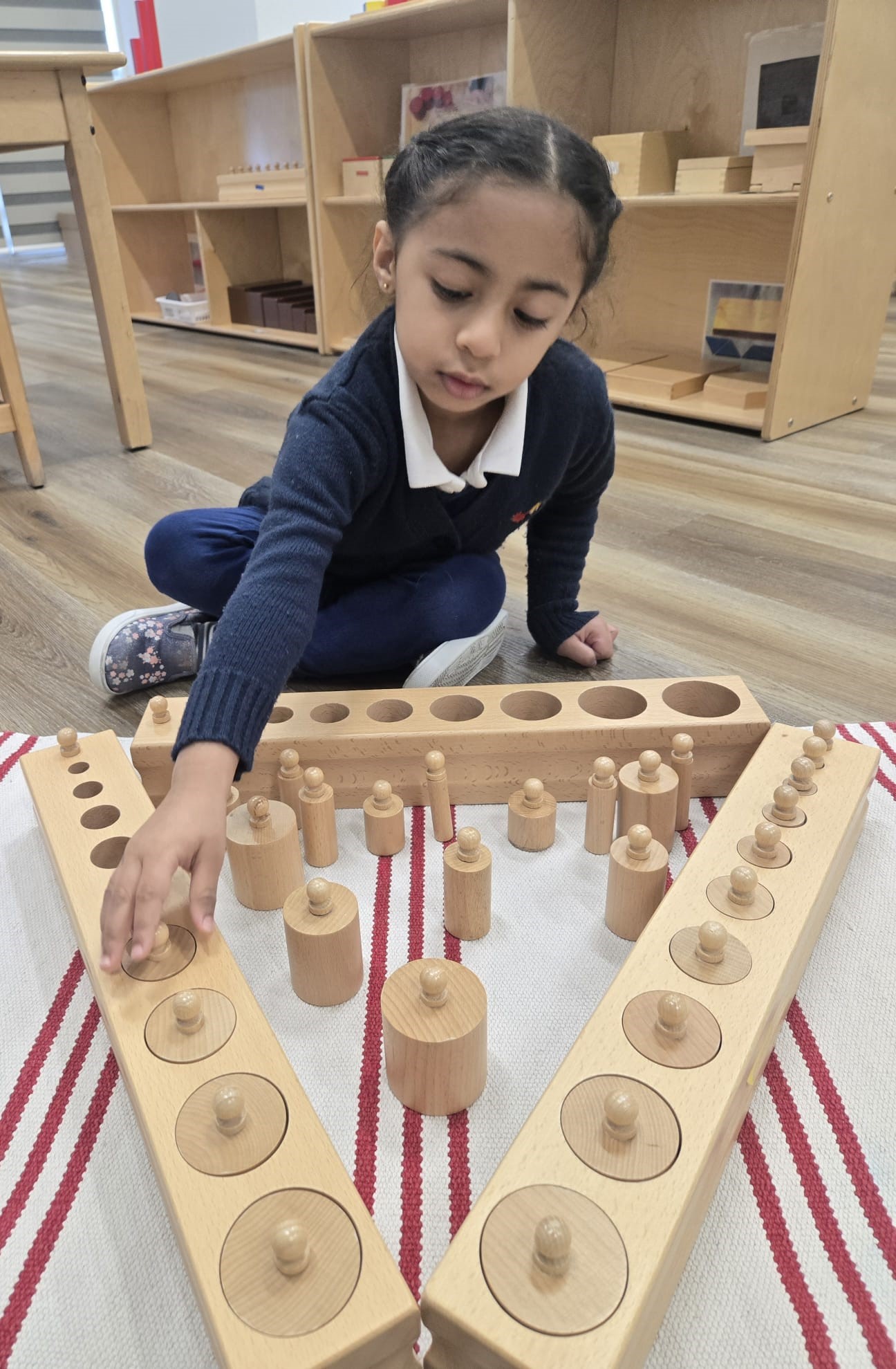 Child working with Montessori knobbed cylinder materials on a floor mat