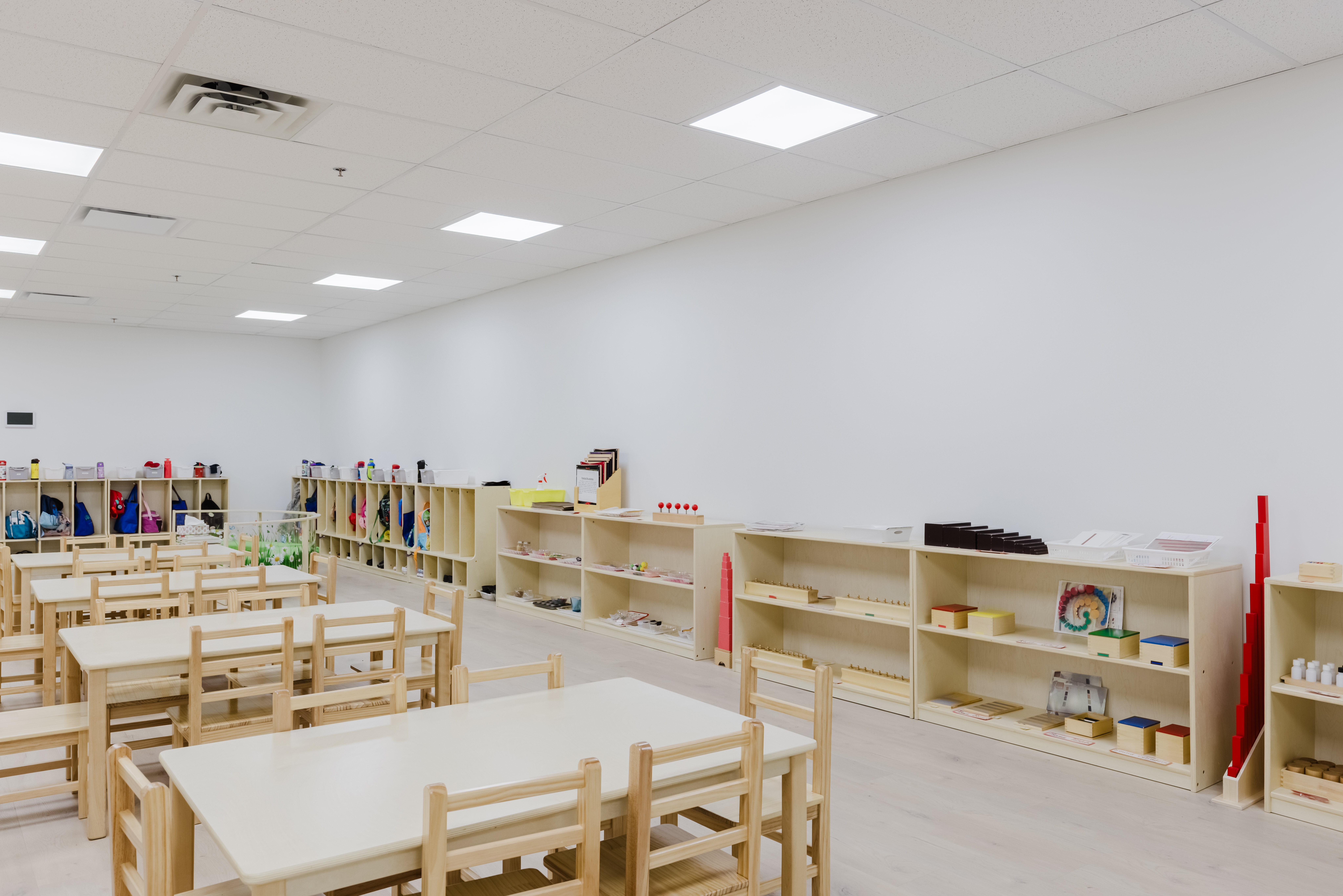 Wide-angle view of Montessori classroom shelving and work tables at Kidzville