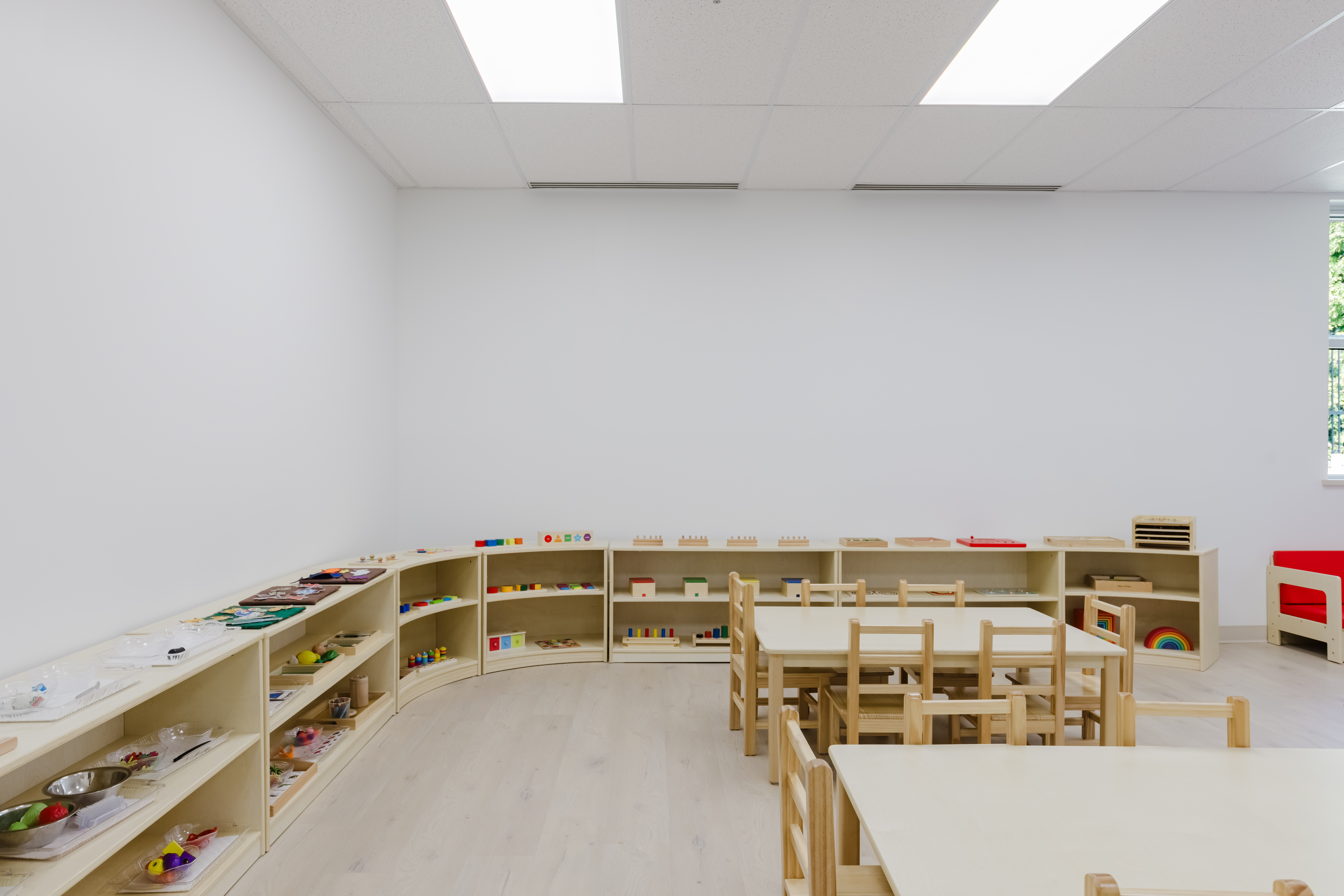 Bright toddler classroom with sunshine rug and Montessori shelves at Kidzville