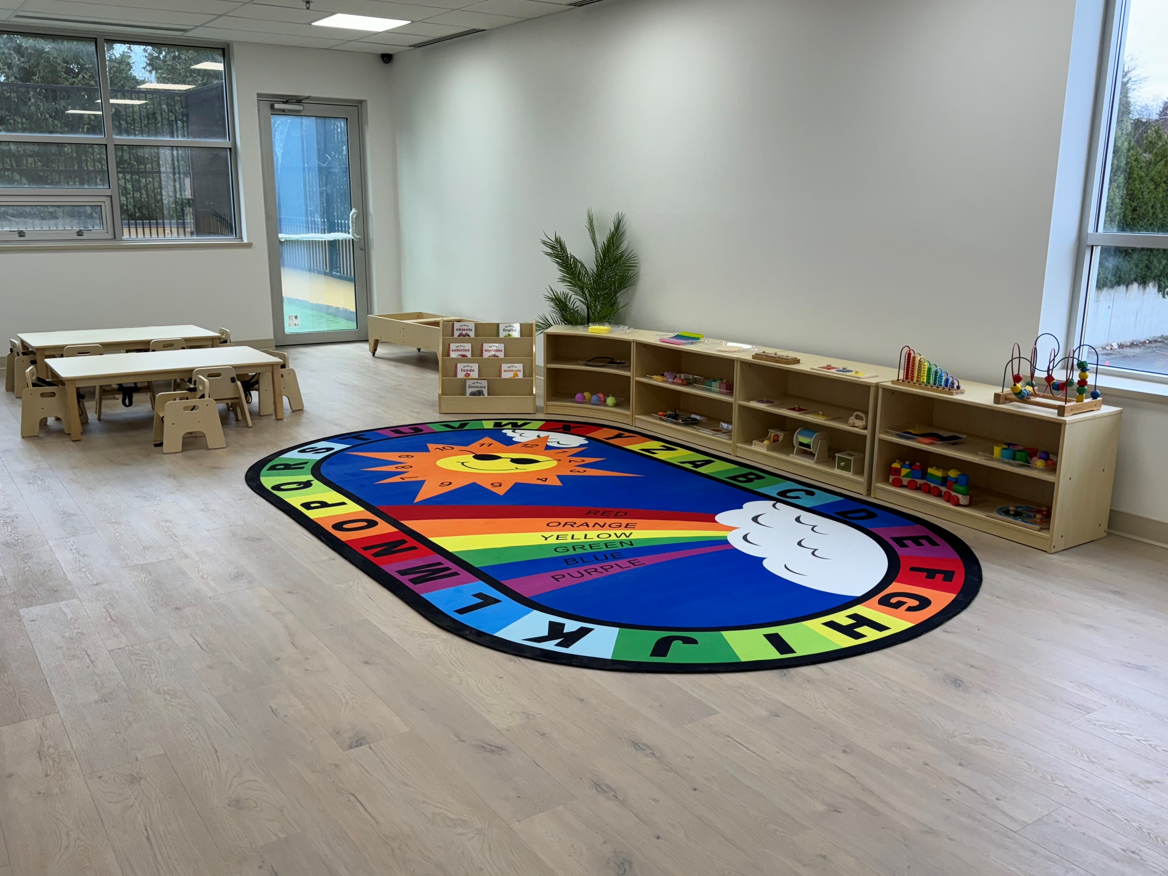 Bright toddler classroom with alphabet rug and wooden shelving at Kidzville