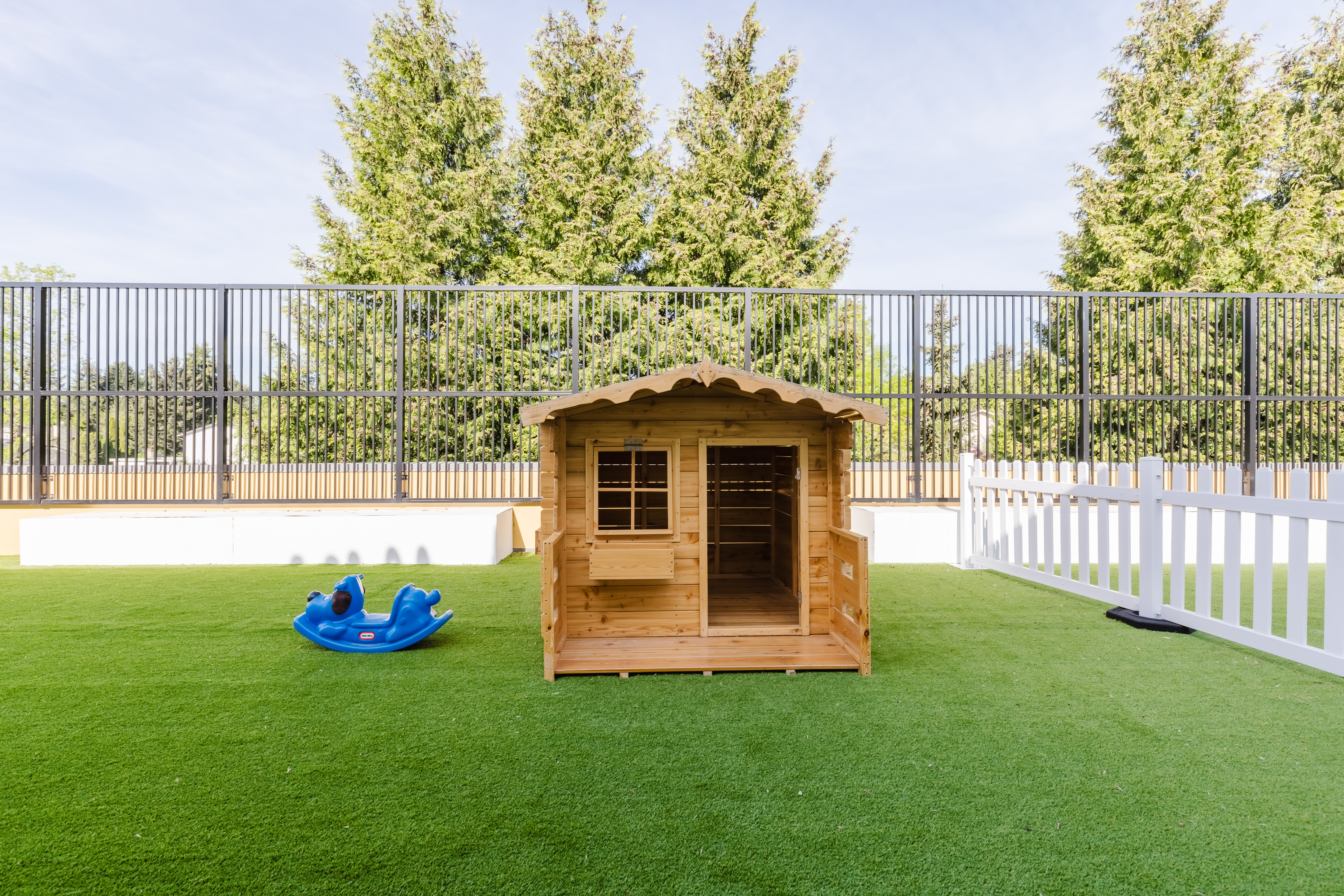 Secure outdoor play area with wooden playhouse and artificial grass at Kidzville