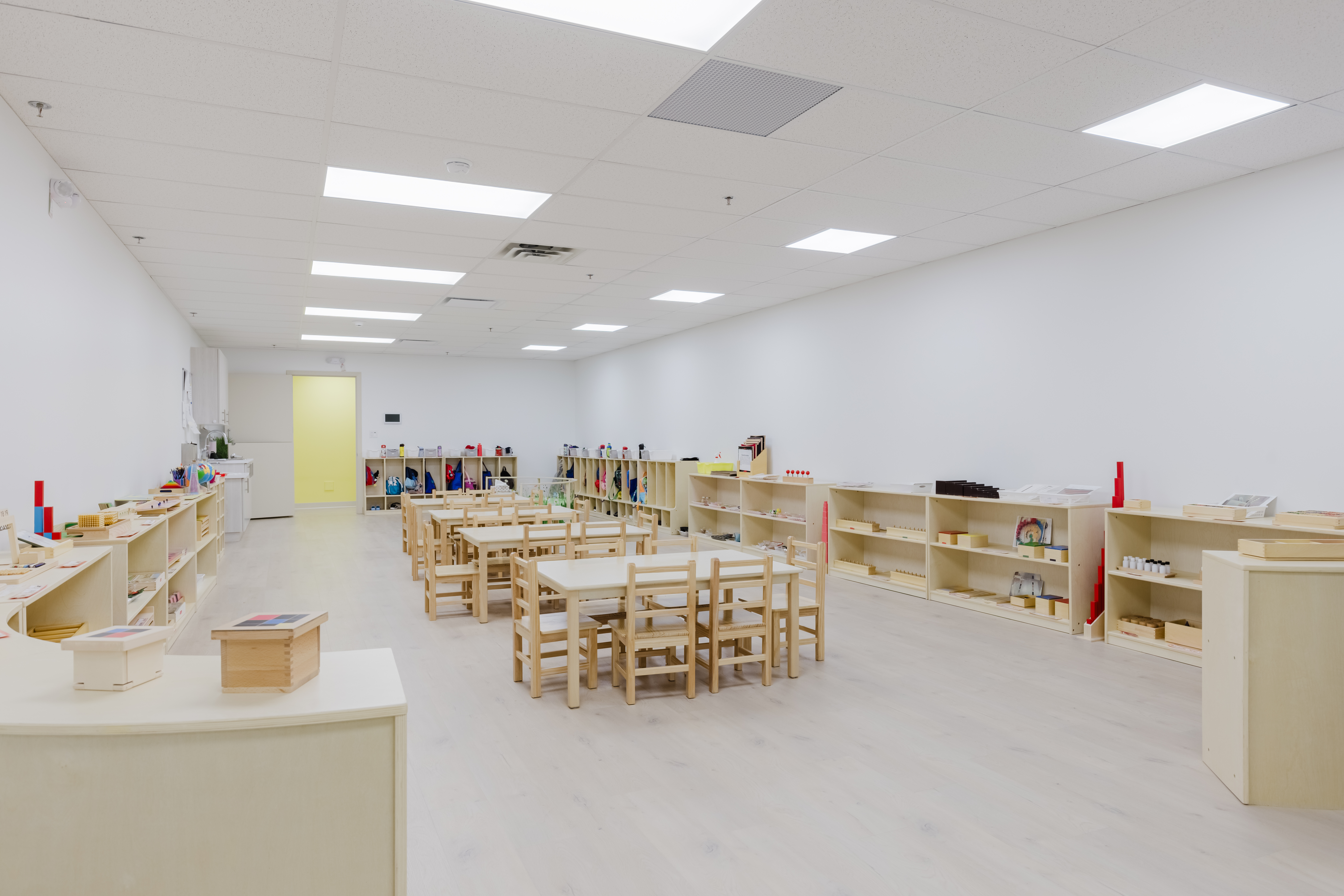 Large Montessori classroom with wooden tables and organised learning shelves at Kidzville