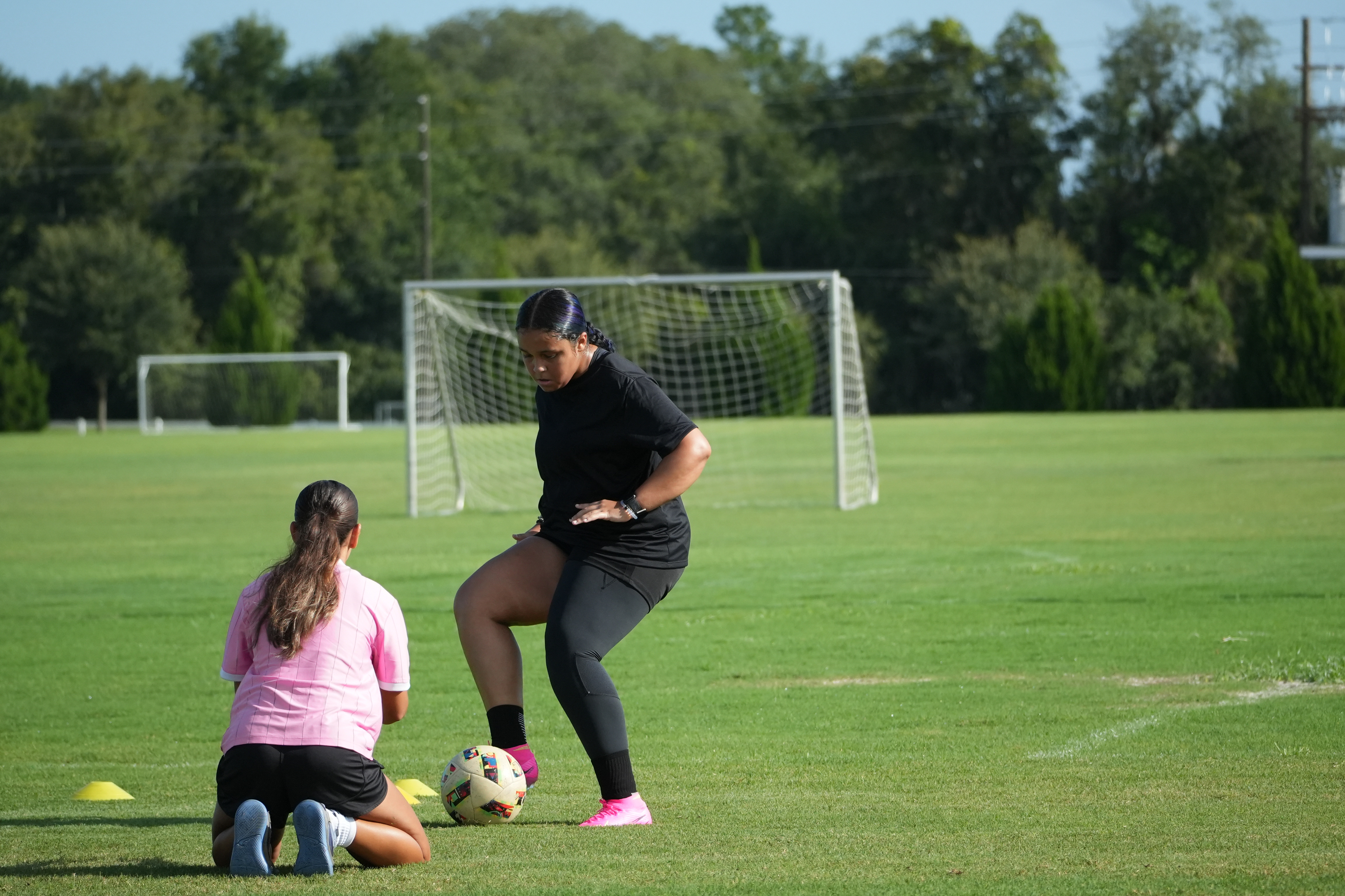 Coach Ana coaching a young female soccer athlete one-on-one on a grass field