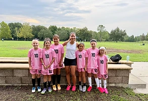 Coach Ana with a group of young female soccer players in pink jerseys