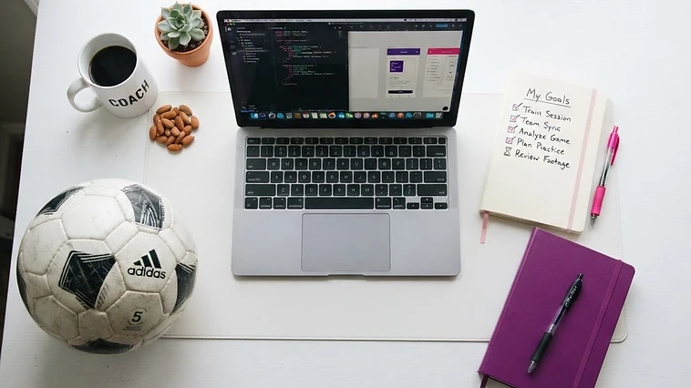 Laptop, checklist notebook and soccer ball on a white desk