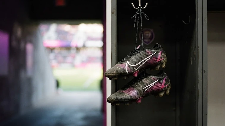 Cleats hanging in a locker with a stadium tunnel in the background