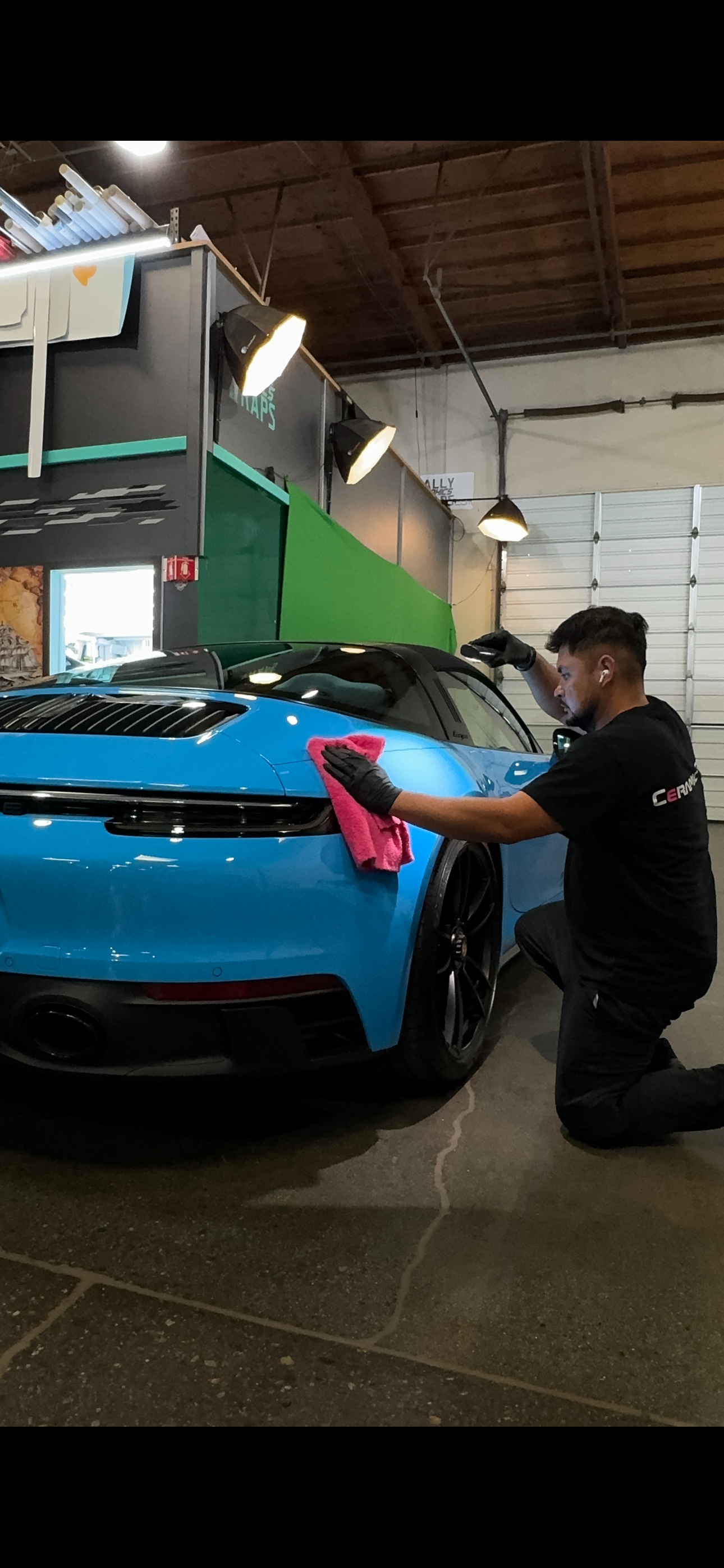 Detailer working on the rear of a bright blue Porsche