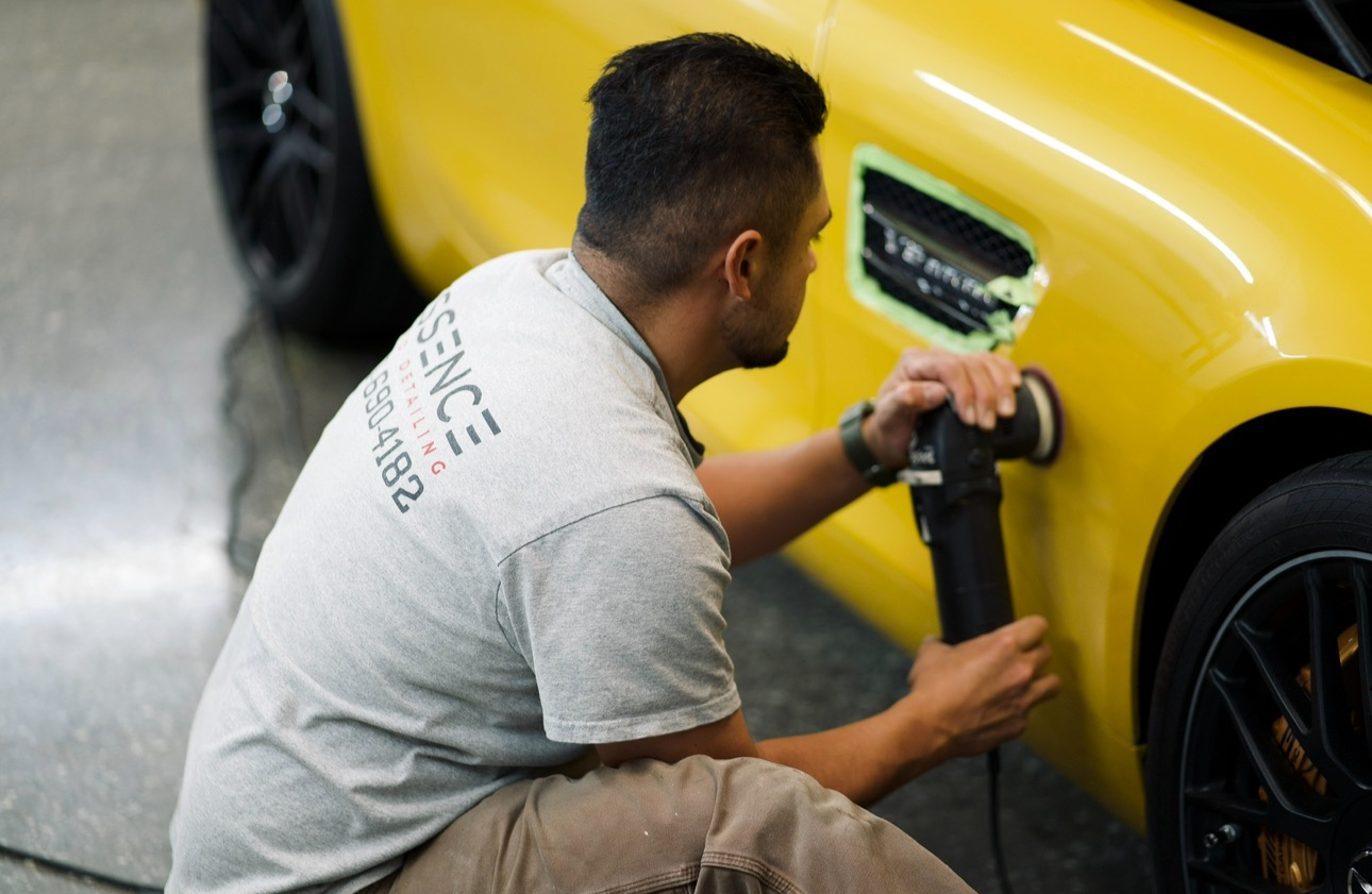 Essence detailer performing paint correction on a bright yellow sports car