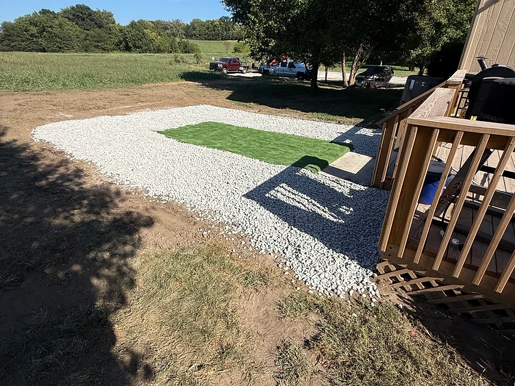 Freshly graded and leveled backyard pad finished with white gravel beside a deck