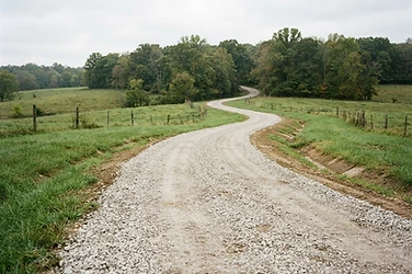 New crowned gravel driveway with graded shoulders curving through rural Missouri property