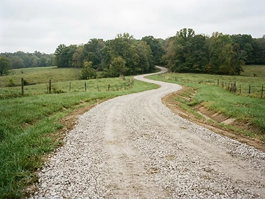 New crowned gravel driveway with graded shoulders curving through rural Missouri property