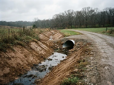 Freshly graded drainage ditch with a culvert pipe along a rural Missouri drive