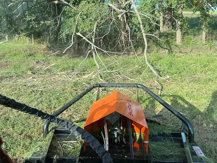 Brush cutter attachment on a track loader clearing downed limbs and underbrush