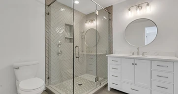 Herringbone tile corner shower with glass enclosure, hexagon mosaic floor, and white vanity