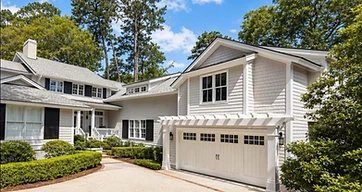 Wide concrete driveway with brick banding leading to a carriage-door garage with pergola