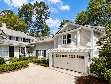 White shingled home exterior with pergola over a carriage-style garage door and concrete driveway
