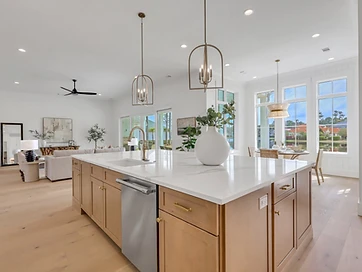 Kitchen island with quartz top and brass pendants looking toward a wall of windows and the living room