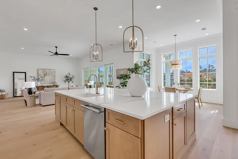 Kitchen island with quartz top and brass pendants looking toward a wall of windows and the living room
