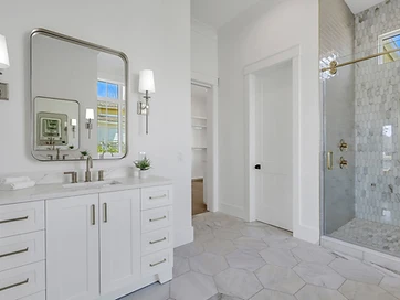 Primary bath vanity with wall sconces, a rounded mirror, and a hexagon tile floor leading to a tiled shower
