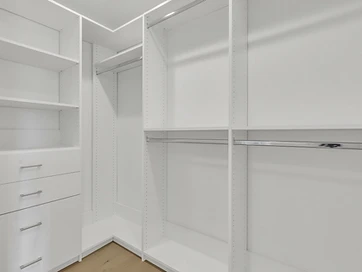 Corner walk-in closet with white shelving, chrome hanging rods, and a bank of drawers