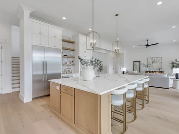 Kitchen island with white quartz top, oak base, brass pendants, and open view to living room
