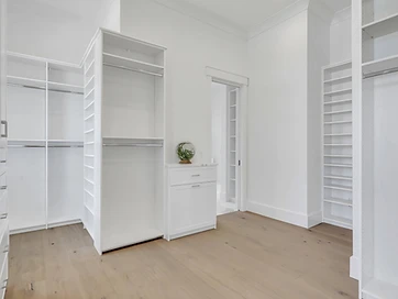 Large walk-in closet with white shelving, hanging sections, shoe shelves, and center drawer unit