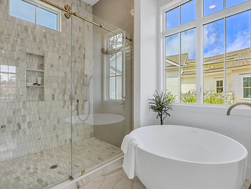 Marble picket tile shower with brass sliding glass door beside a round freestanding tub