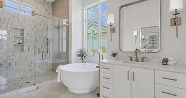 Primary bath with round tub, brass fixtures, marble picket tile shower, and white vanity with sconces