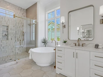 Primary bath with round tub, brass fixtures, marble picket tile shower, and white vanity with sconces