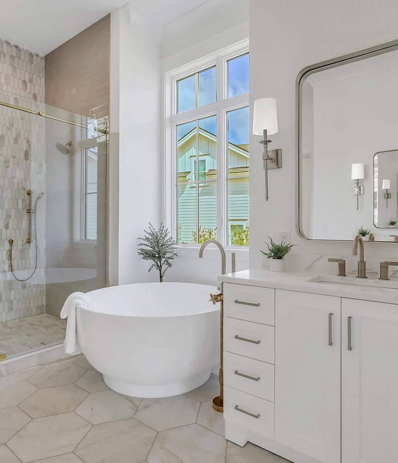 Primary bath with round tub, brass fixtures, marble picket tile shower, and white vanity with sconces