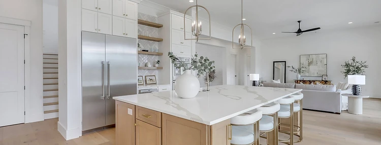 Open white kitchen with quartz island, oak cabinetry, and adjoining living room