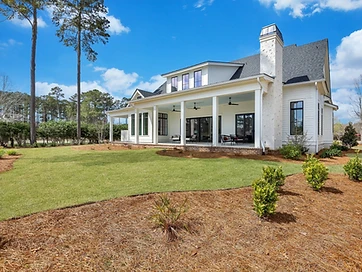 Rear view of a white two-story home with a covered porch and a shell-stucco chimney