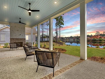 Covered porch with a painted plank ceiling, ceiling fans, and an outdoor fireplace overlooking the water