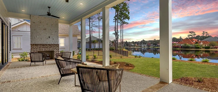 Covered porch with a painted plank ceiling, ceiling fans, and an outdoor fireplace overlooking the water