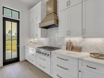 Kitchen range wall with brass hood, gas cooktop, white shaker cabinets, and herringbone tile