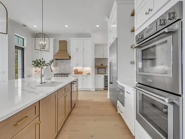 Kitchen with stainless double wall ovens, oak island, and brass range hood in the background
