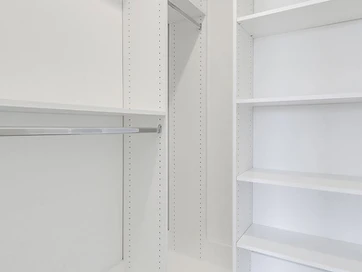 White closet shelving and hanging rods with a light wood-tone floor