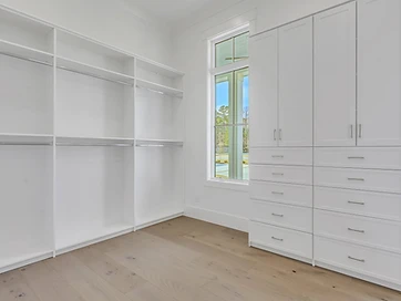 Walk-in closet with white shelving, hanging rods, and built-in drawer cabinetry beside a window