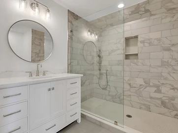 Bathroom with marble-look subway tile shower, glass panel, round mirror, and white vanity